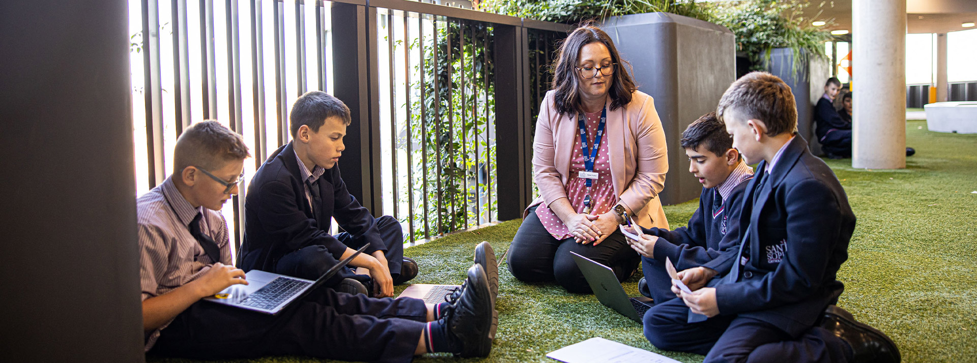 Santa Sophia Catholic College Box Hill students sitting with dedicated teacher on astroturf