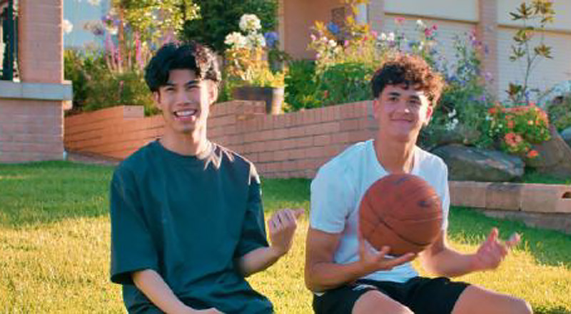 Two teenagers playing basketball and giving the thumbs up